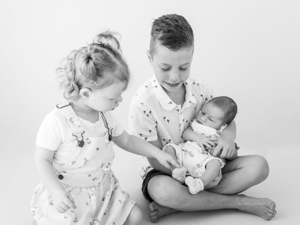 Black and white image of a sibling affectionately holding their new baby brother.