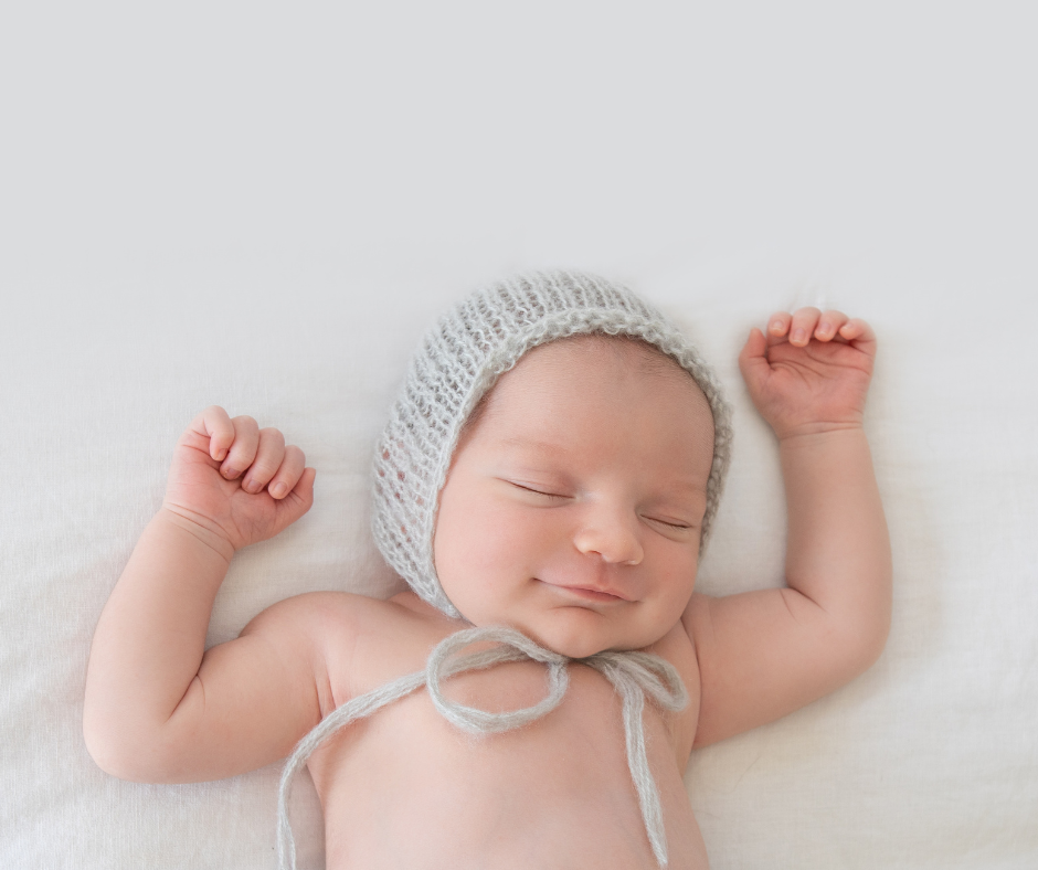 newborn sleeping with smile on his face and his arms raised above his head.